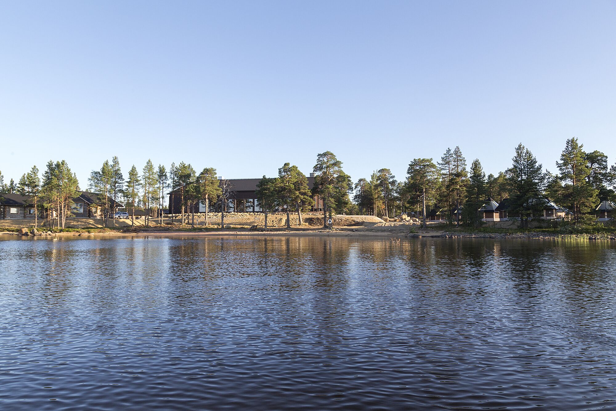 A lakeside cabin with a dock, surrounded by trees and a clear sky.