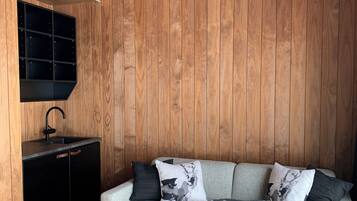 Ein modernes Wohnzimmer mit grauem Sofa, schwarz-weißen Kissen, einem schwarzen Couchtisch und einer Holzwand mit integriertem Regal.