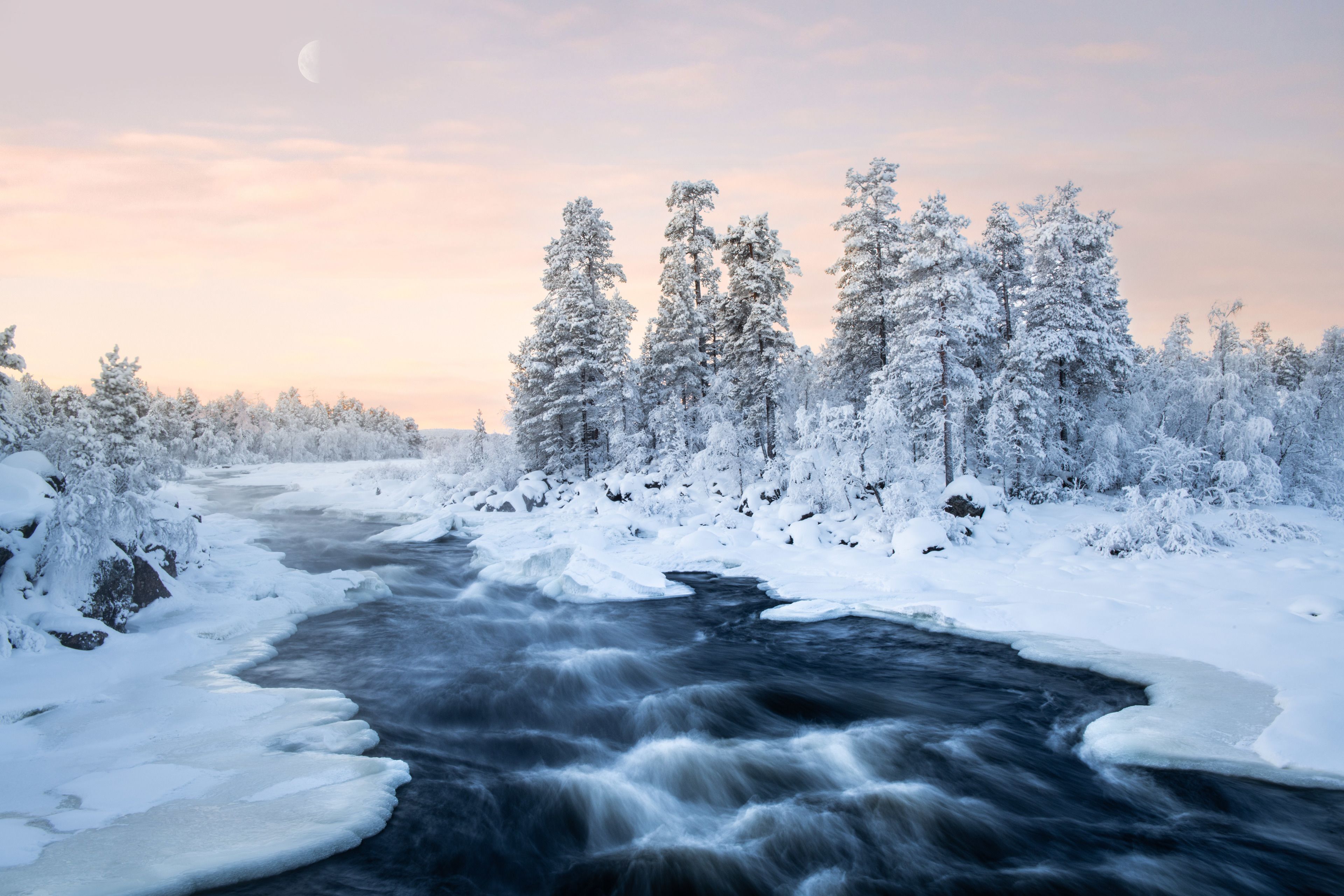 A river flowing through a snowy forest with trees on both sides.