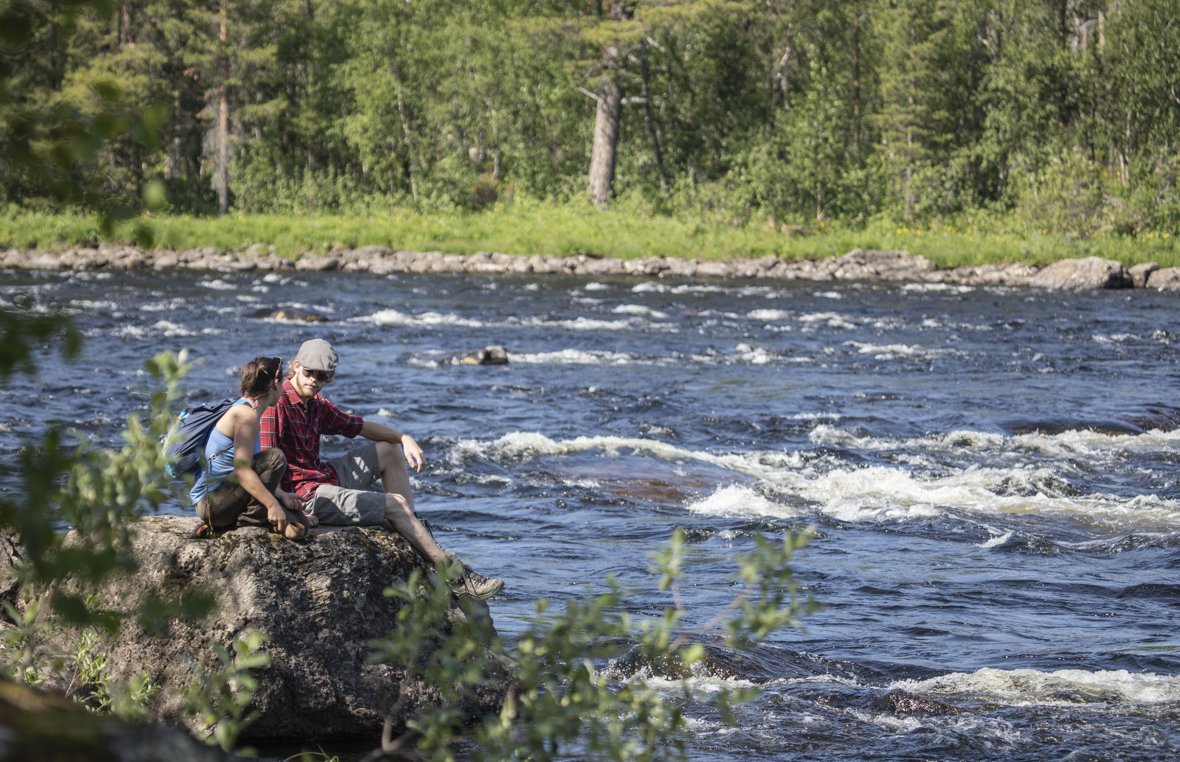 Two people sitting on a rock by a river.