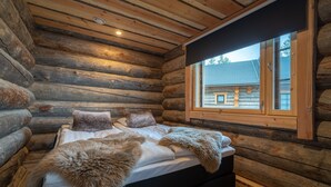A log cabin bedroom with a bed, fur throw blankets, and a window with a view of a house.
