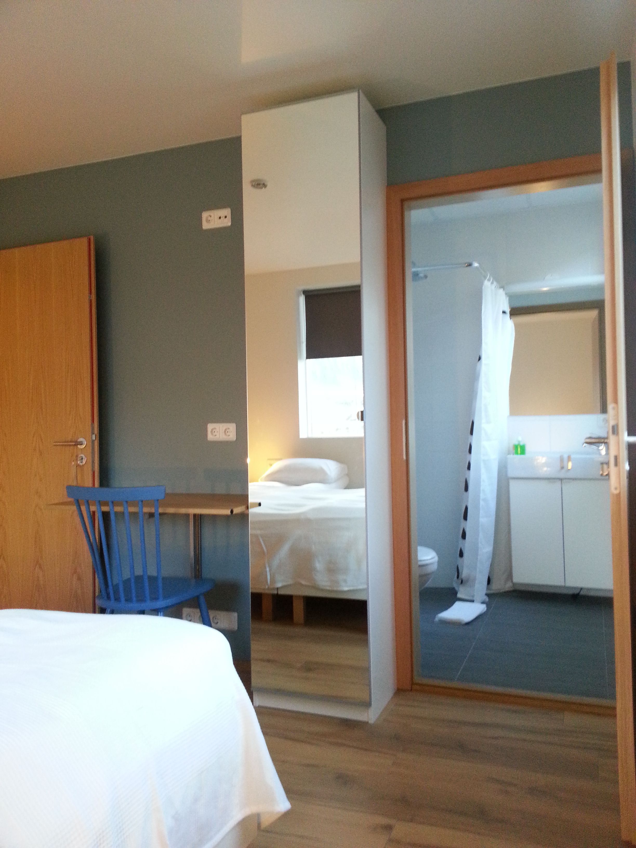 Habitación de hotel con cama, escritorio, silla, baño con ducha y pequeña cocina.