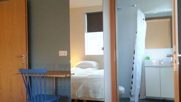 Habitación de hotel con cama, escritorio, silla, baño con ducha y pequeña cocina.