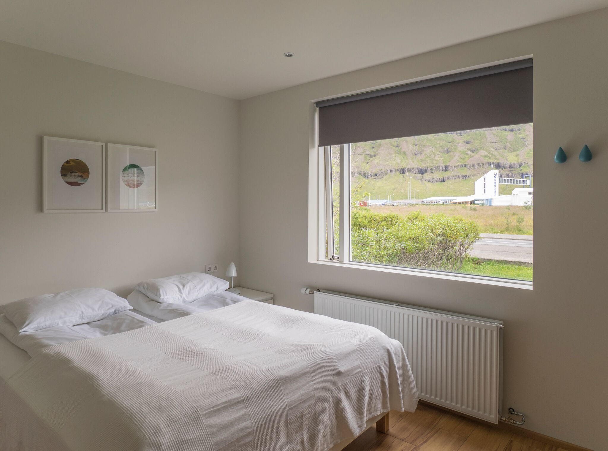 Ein Schlafzimmer mit großem Fenster, einem Bett, einem Nachttisch und einer Heizung.