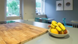 A modern dining area with a wooden table, a bowl of fruit, and blue chairs. - Seyðisfjörður Guesthouse (Seydisfjordur)