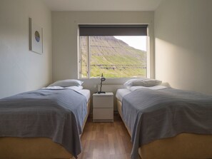 A room with two beds, a nightstand, and a window with a view of a green landscape. - Seyðisfjörður Guesthouse (Seydisfjordur)