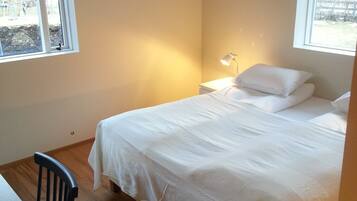 A bedroom with a bed, a desk, and a chair. There are windows on two sides of the room.