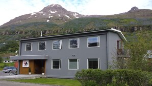 A modern guesthouse with a flat roof, large windows, and a sign indicating it is a guesthouse and post-house. - Seyðisfjörður Guesthouse (Seydisfjordur)