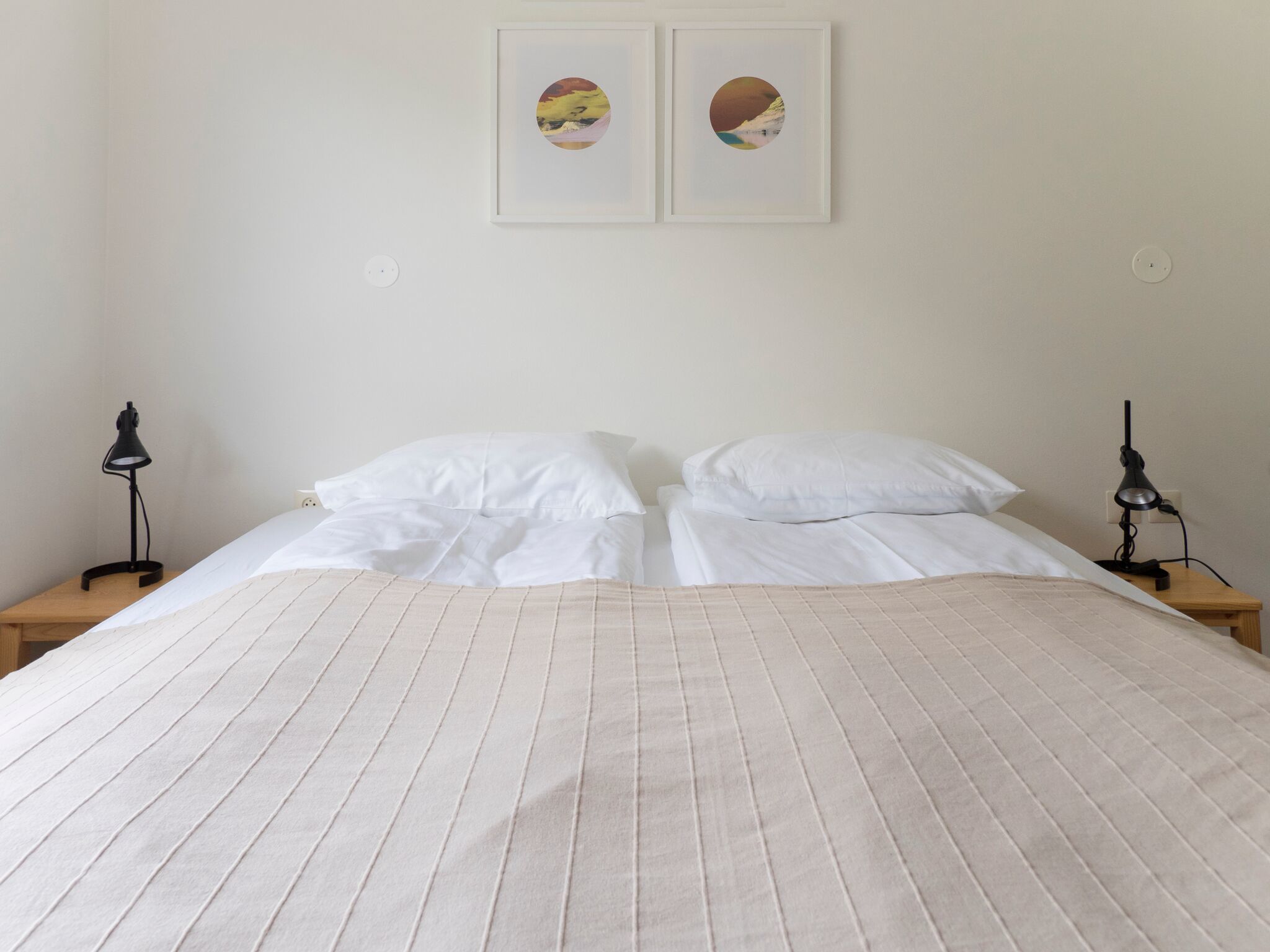 Una cama bien hecha con una colcha a rayas, dos mesitas de noche con lámparas y dos cuadros enmarcados en la pared.