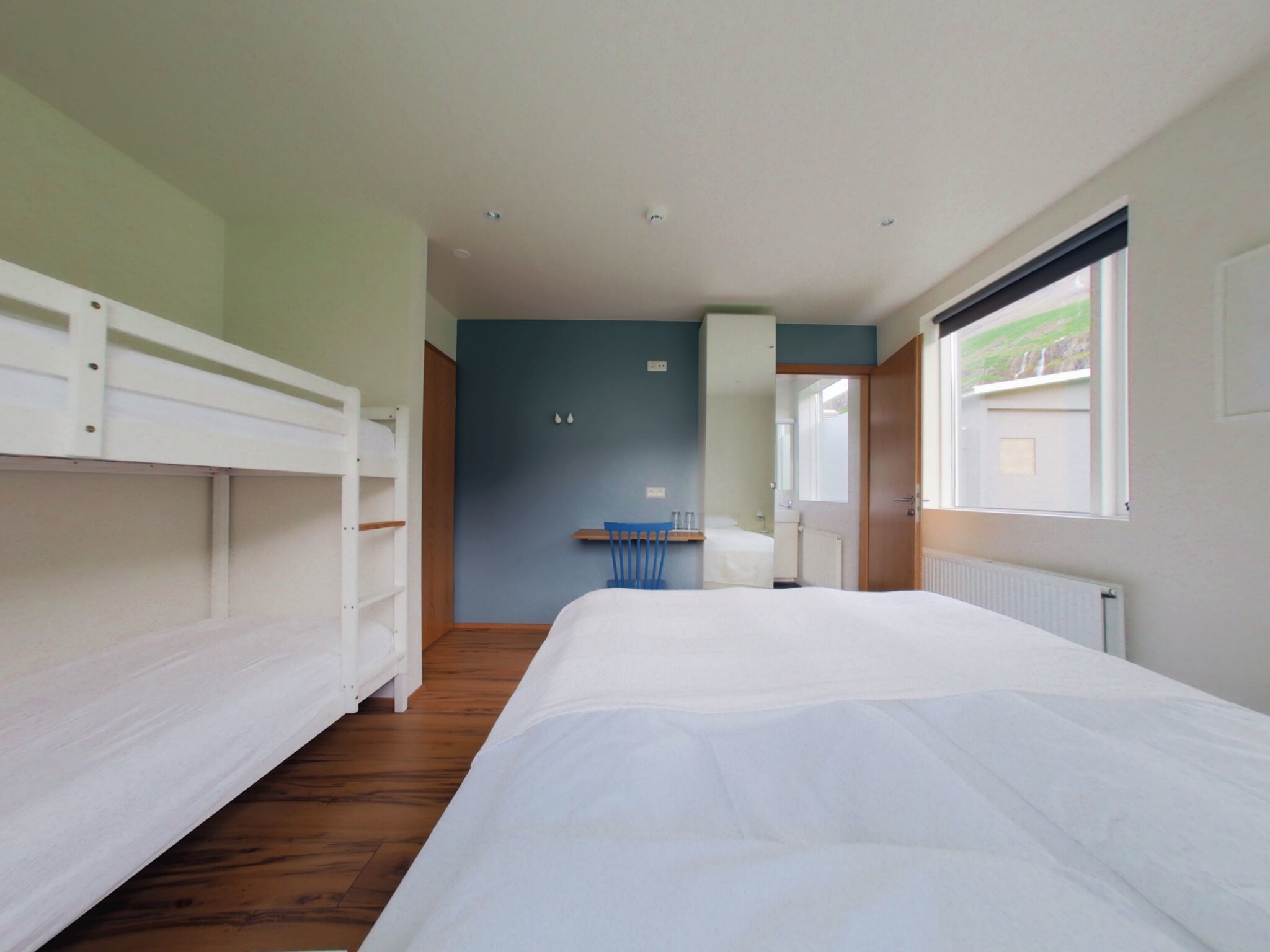 A bedroom with bunk beds, a single bed, a window, and a bathroom visible through an open door.