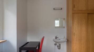 A small, compact room with a wooden cabinet, a white sink, a mirror, a red chair, and a table.