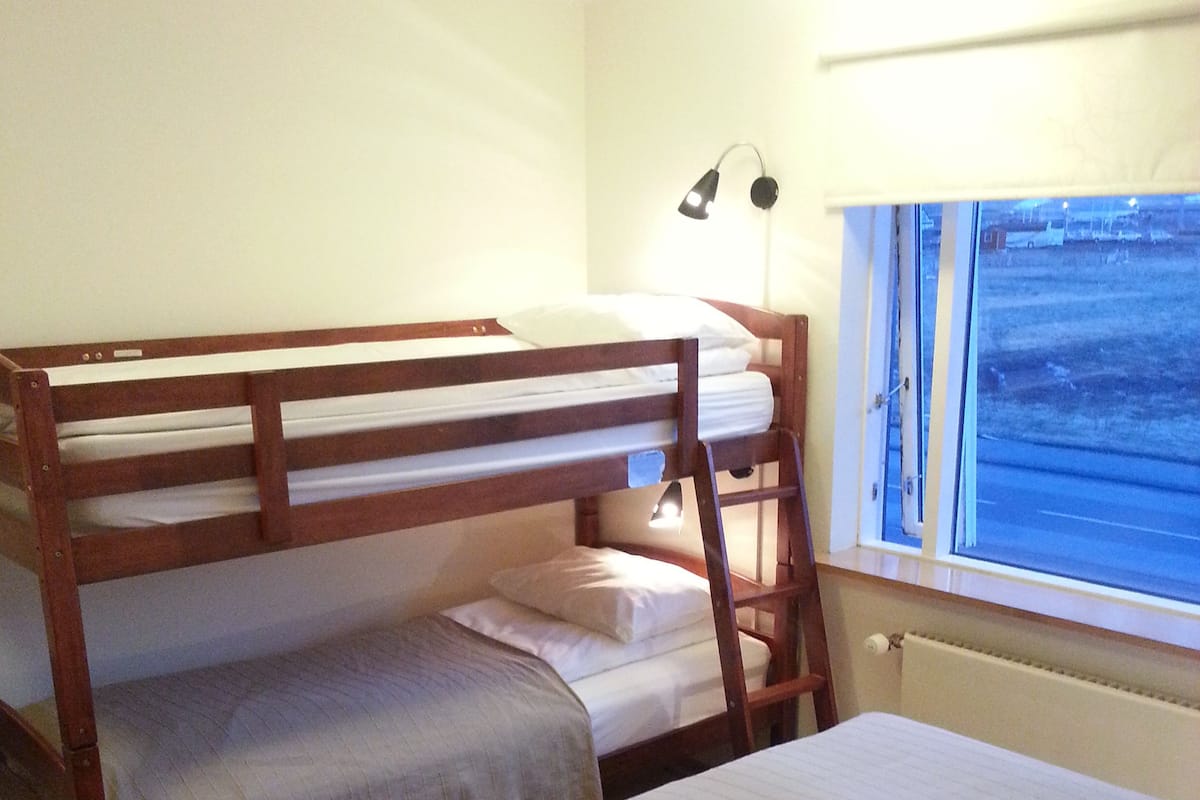 Quarto com duas camas de solteiro sobrepostas, uma janela com vista e uma luminária de cabeceira.