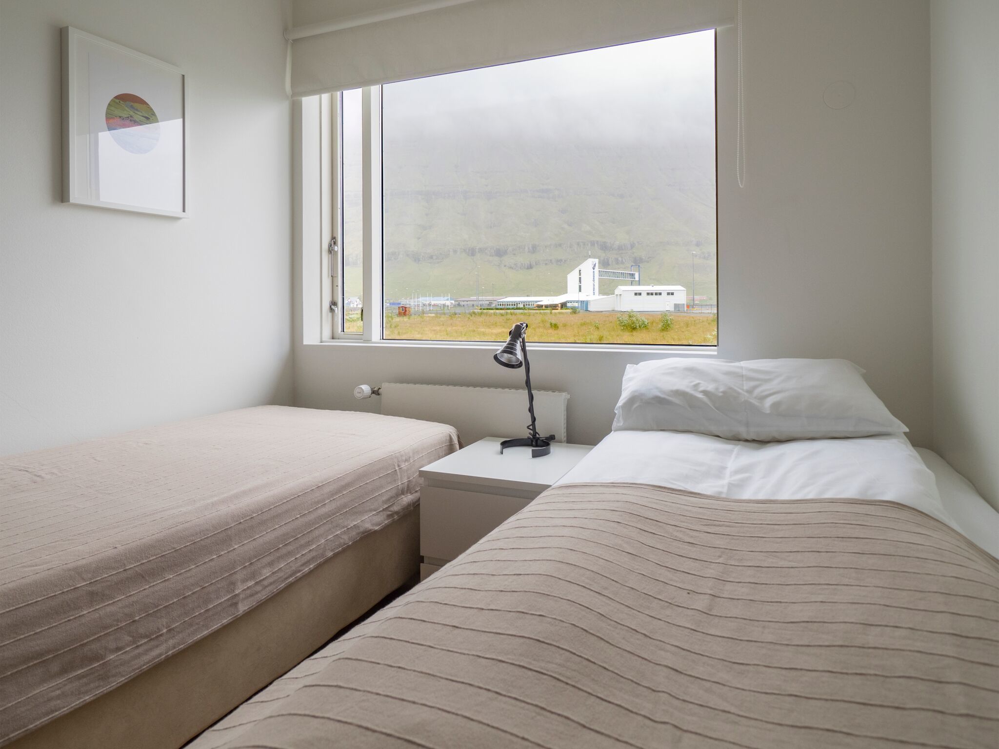 Una camera da letto con due letti, un comodino, una lampada e una finestra vista edificio e paesaggio.