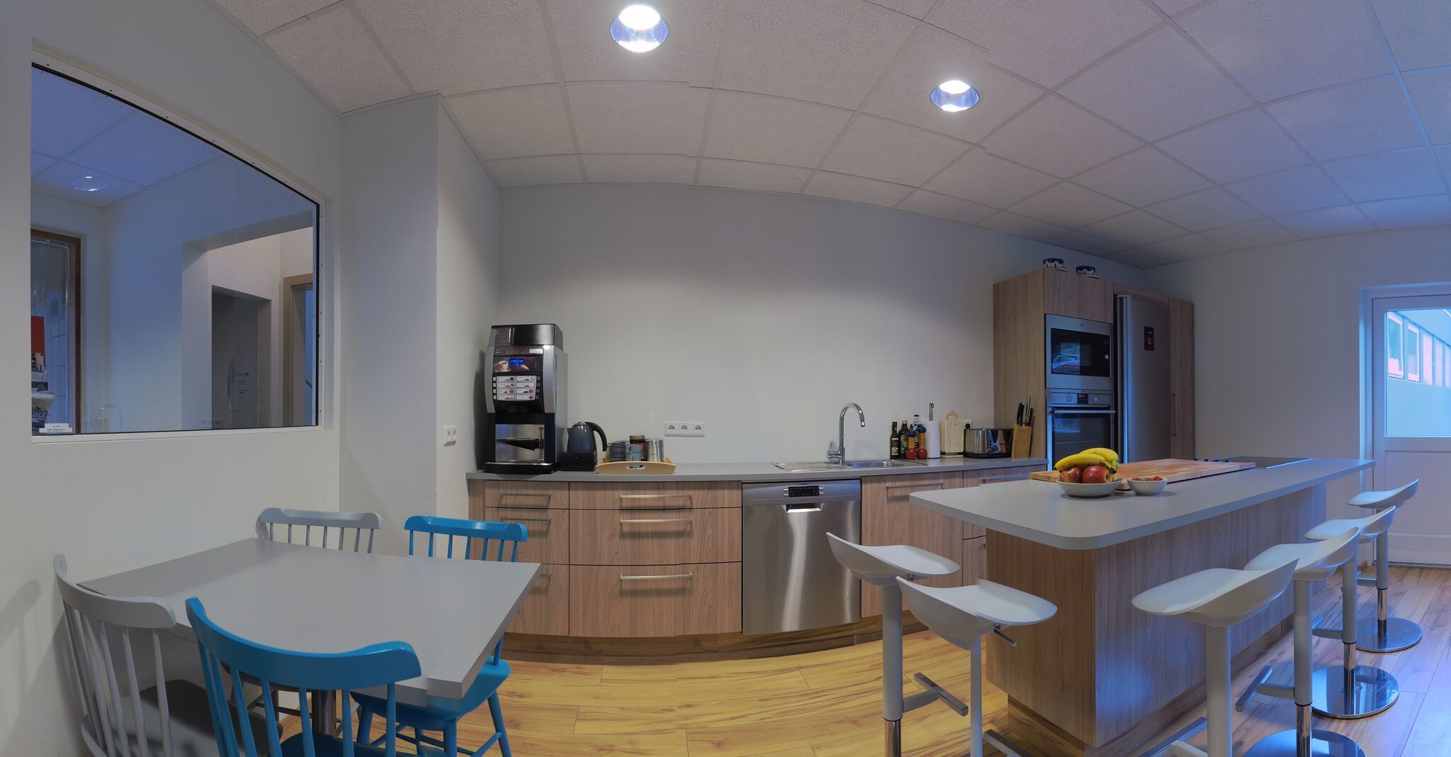Una cocina moderna con una isla central, electrodomésticos integrados y un comedor con sillas azules.