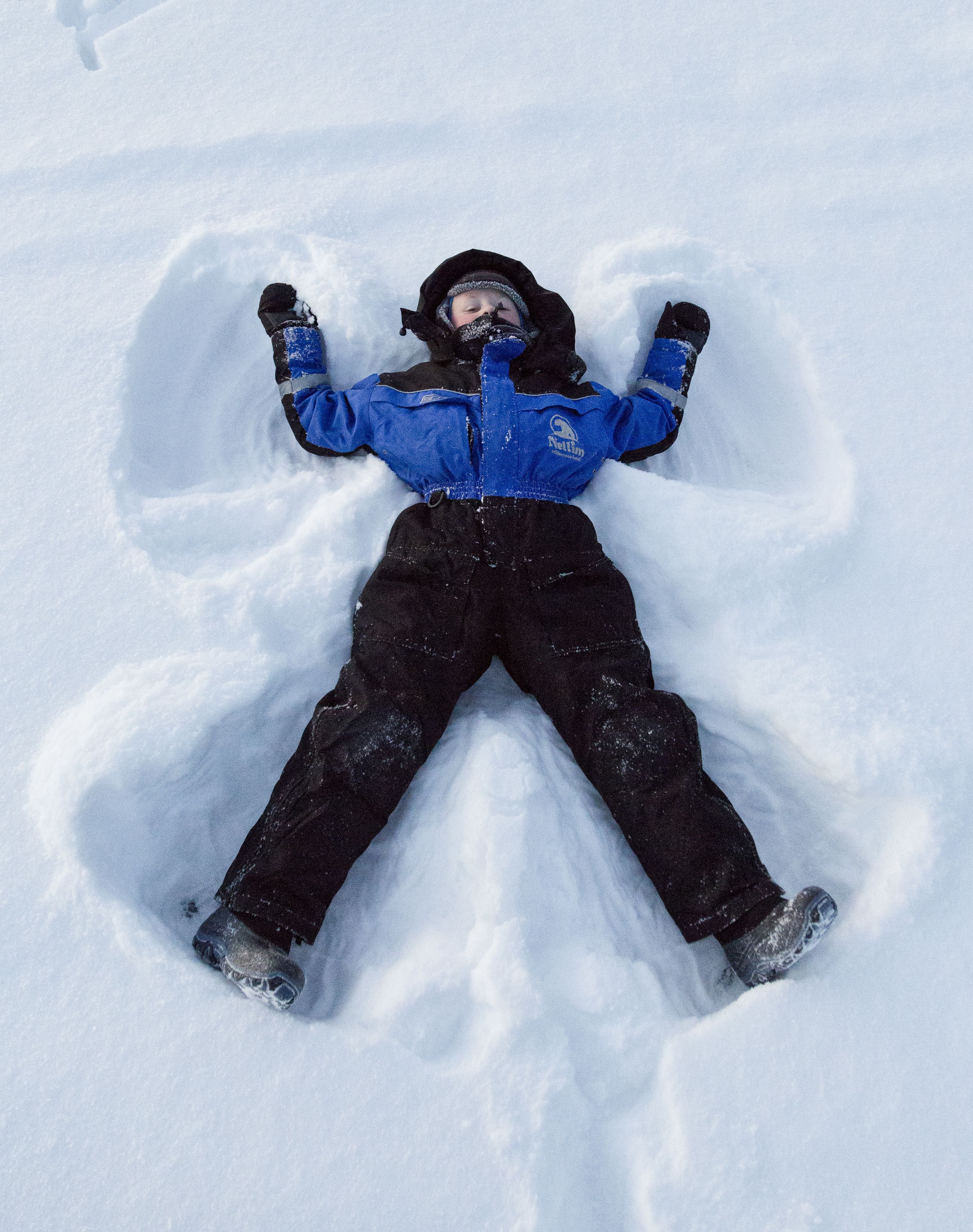 Criança deitada na neve, formando um anjo de neve.