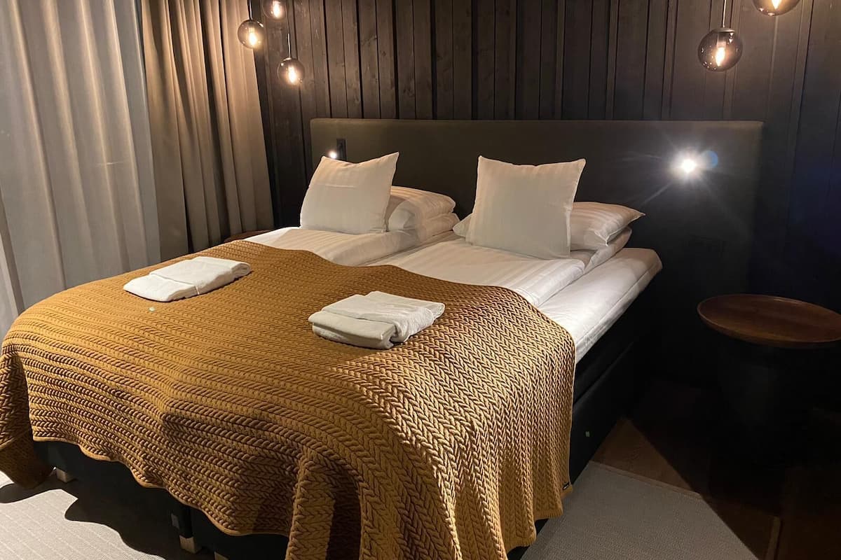 Un lit bien fait, avec une couverture marron tissée, des oreillers blancs et une tête de lit en bois.
