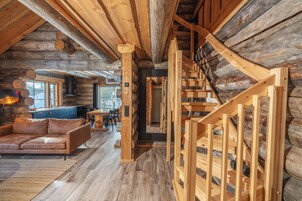 Interior de uma cabana de tronco com escada de madeira, um sofá e uma área de jantar.