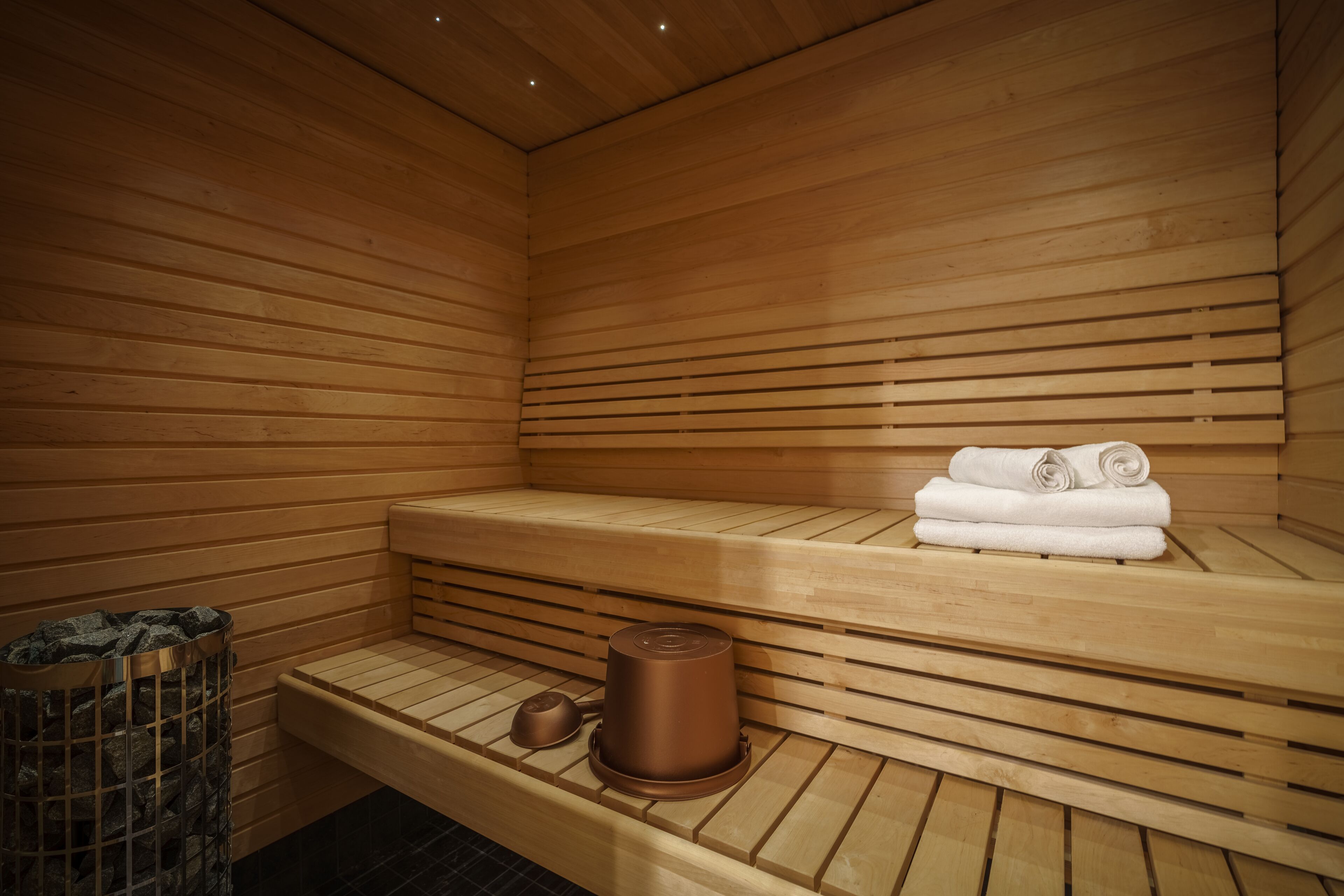Una sauna con bancos de madera, una pila de toallas y un recipiente metálico.