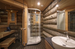 A log cabin bathroom with a glass-enclosed shower, a wooden bench, and a large sink.