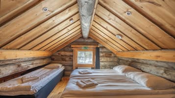 A log cabin with a sloped ceiling, two beds with towels, a window, and a door with an exit sign.