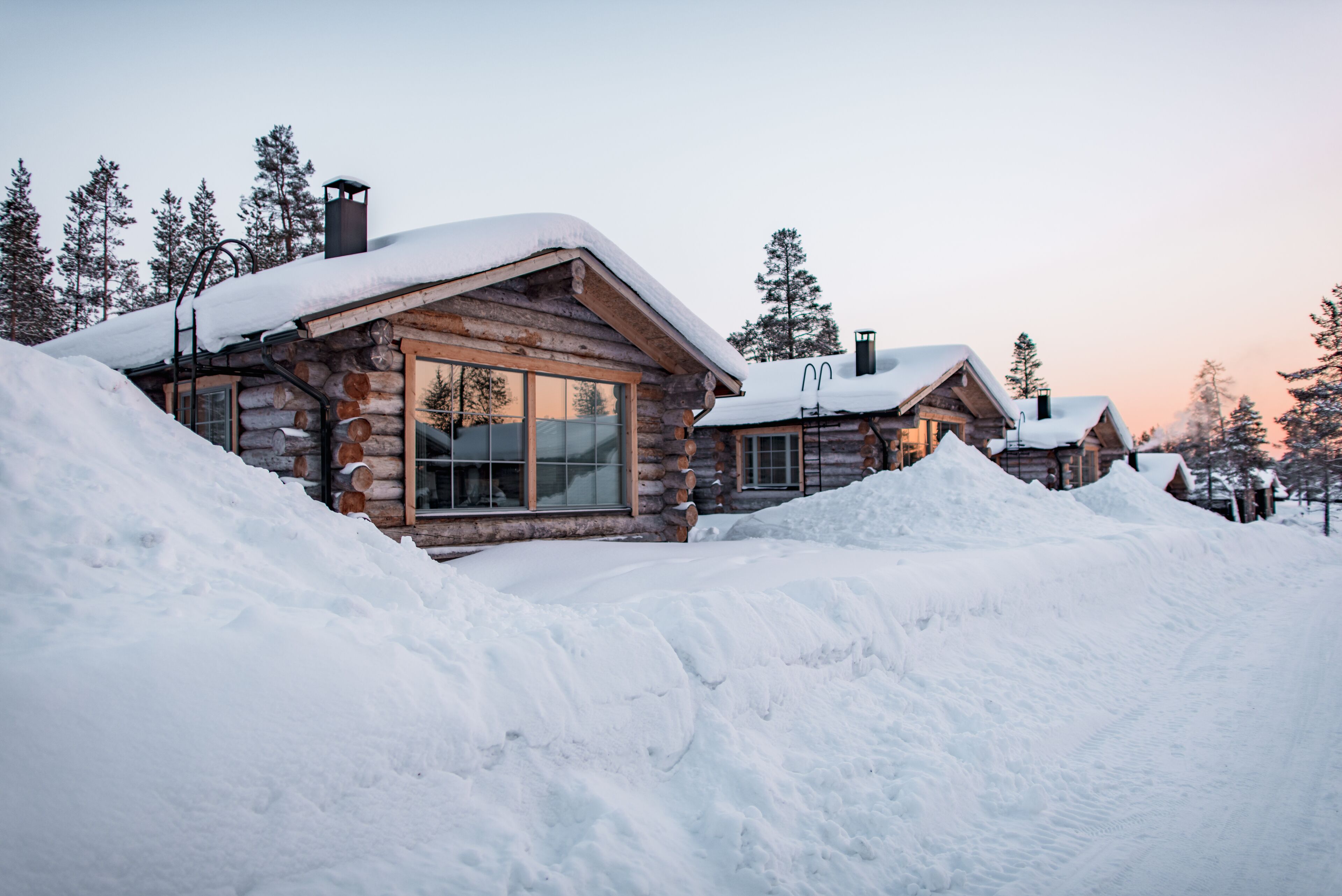 Una cabaña de troncos con un amplio ventanal, rodeada de nieve.