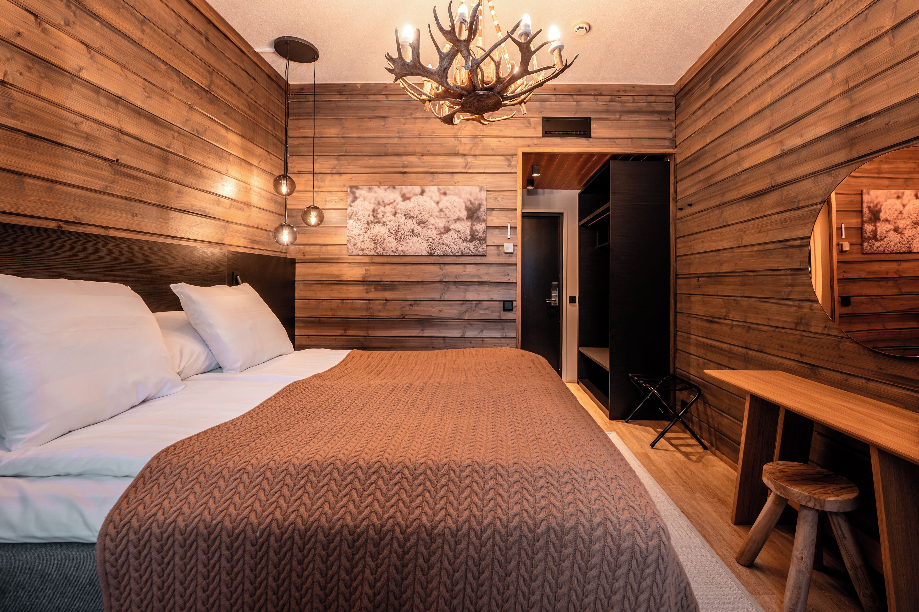 Een moderne slaapkamer met houten lambrisering, een groot bed met witte lakens, een kroonluchter en een houten bureau met krukje.