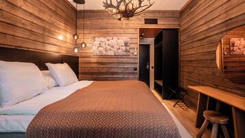 Een moderne slaapkamer met houten lambrisering, een groot bed met witte lakens, een kroonluchter en een houten bureau met krukje.