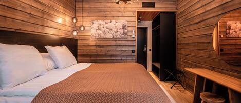 A modern bedroom with wooden paneling, a large bed with white linens, a chandelier, and a wooden desk with a stool.