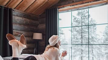A cozy cabin room with a bed, a window with a view of trees, and a lamp.