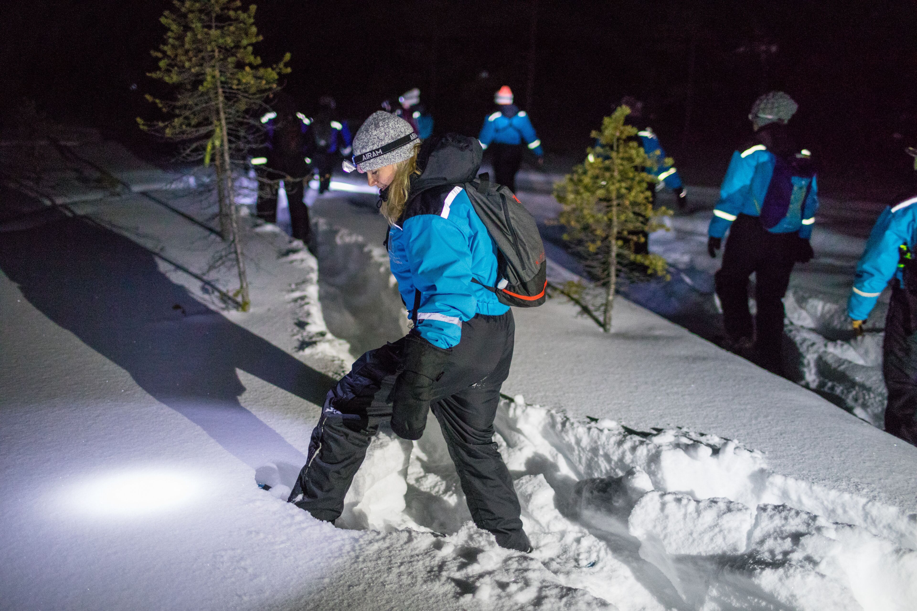 A group of people in blue jackets and helmets, engaged in snowboarding on a snowy slope at night.