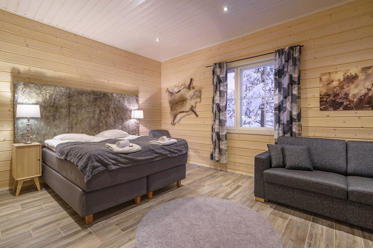 Une chambre située dans un chalet en rondins, avec un lit, un canapé, un tapis et une œuvre d’art accrochée au mur.