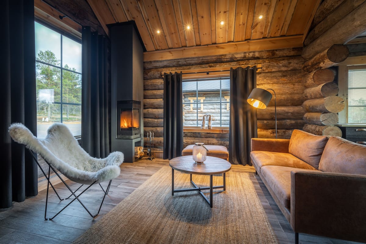 L’intérieur d’un chalet confortable, avec une cheminée, un fauteuil en fourrure blanche, un canapé et une table basse ronde.