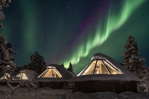 Paisagem nevada com várias cabanas de madeira, cada uma com telhado triangular e luz interior visível.