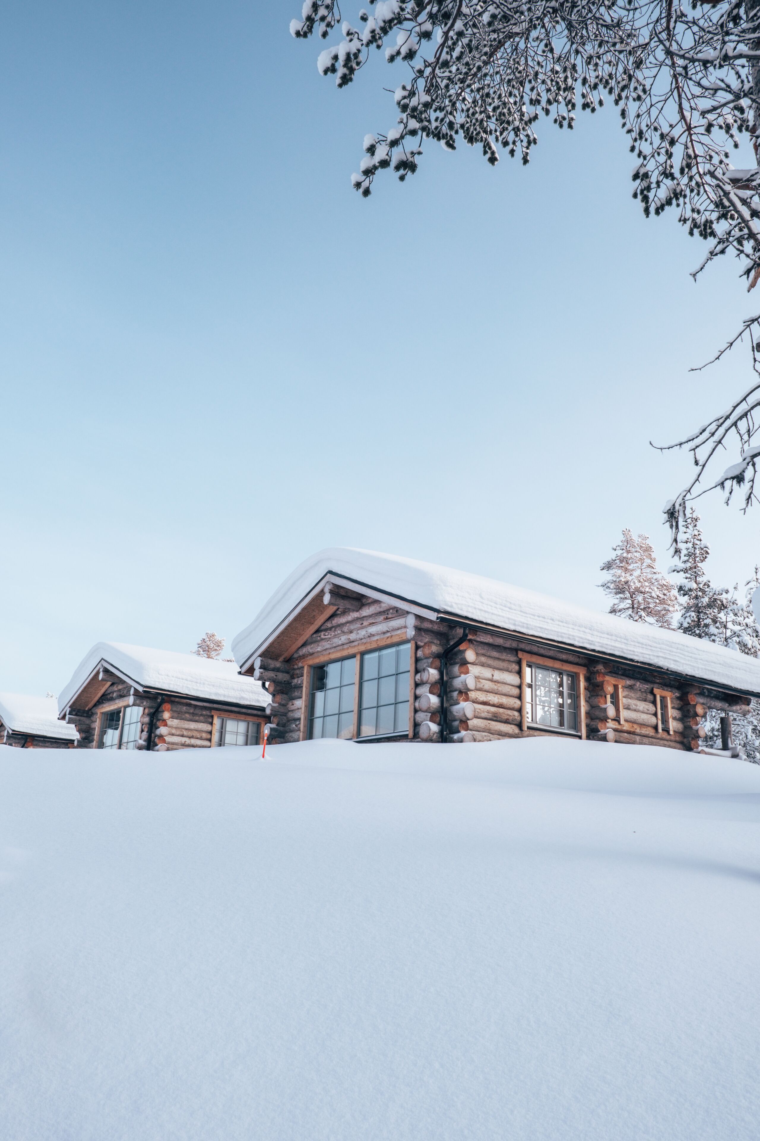 A log cabin with a snow-covered roof and windows, surrounded by a snowy landscape.