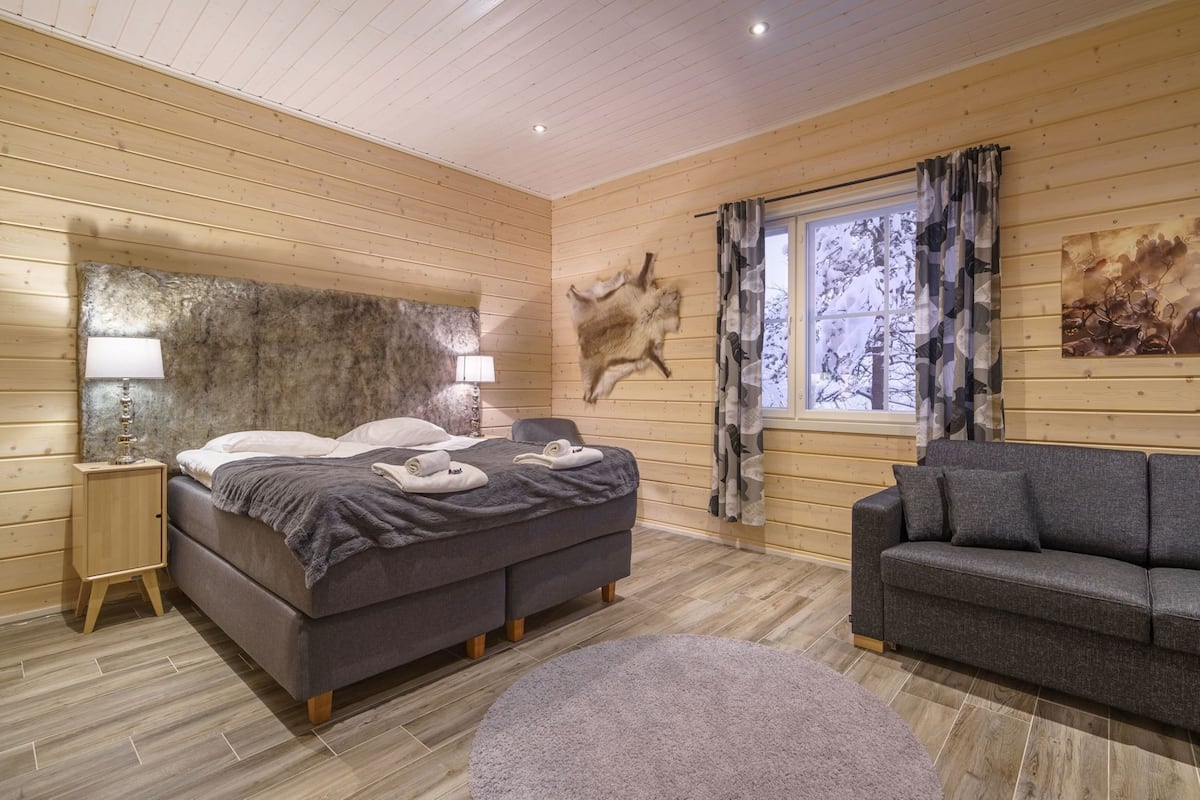 Une pièce comprenant un lit, un canapé, une fenêtre avec des rideaux, une lampe fixée au mur et un tapis en fourrure.