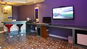 Un área de bar con mostrador, dos taburetes, un televisor montado en la pared y suelo de baldosas.