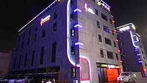 Un hotel de varios pisos con diseño moderno, que destaca un llamativo letrero de neón y una amplia entrada.