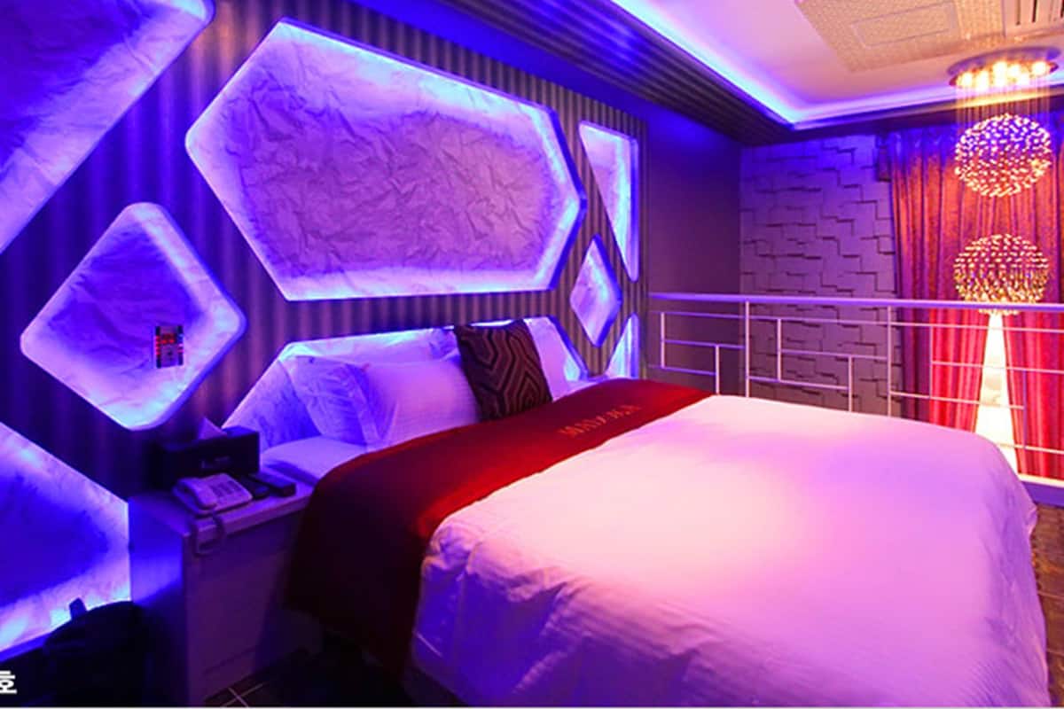 A modern hotel room with a large bed, a nightstand, and a wall-mounted light fixture.