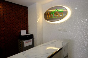 A reception desk with a marble top, a wall-mounted sign for 'Wai Wai' hotel, and a patterned wall behind the desk.