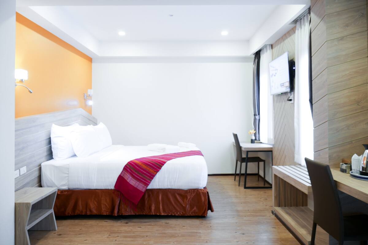 A hotel room with a bed, a desk, a chair, a TV, and a window.