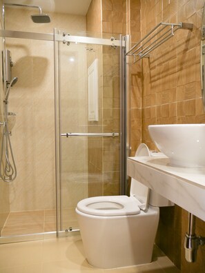 Un baño moderno con cabina de ducha de vidrio, inodoro blanco y un lavamanos grande.