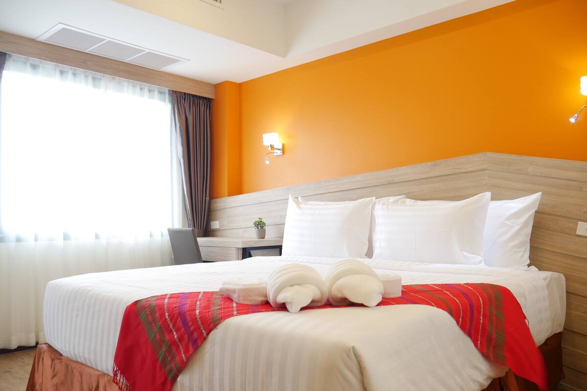 A hotel room with a large bed, a desk, and a window with curtains.