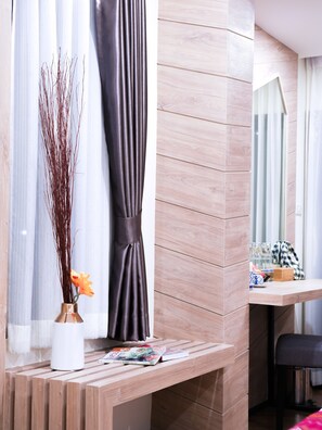 Una habitación moderna con un banco de madera, un jarrón con ramas y flores, una cortina oscura y un espejo que refleja una ventana con cortinas.