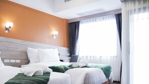 Ein Hotelzimmer mit zwei Betten, einem Holzkopfende, einem großen Fenster mit Vorhängen und Wandleuchten.