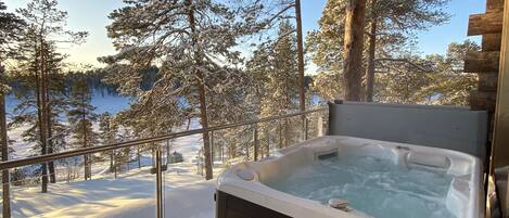 A hot tub on a wooden deck with a snowy landscape and trees in the background.