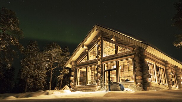 A log cabin with large windows, surrounded by snow-covered ground and trees, under a night sky with visible stars. - Wilderness Hotel Nangu & Igloos (Inari)