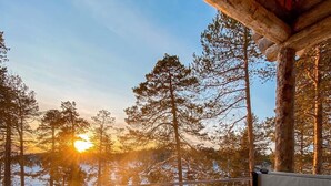 A hot tub with a person relaxing, surrounded by snow and trees, with a sunset in the background. - Wilderness Hotel Nangu & Igloos (Inari)