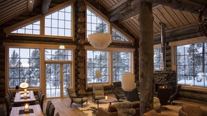 A cozy log cabin interior with large windows, a stone fireplace, and comfortable seating areas. - Wilderness Hotel Nangu & Igloos (Inari)
