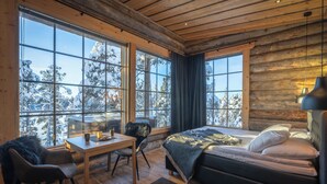 A cozy log cabin room with a large bed, a desk, and a chair. - Wilderness Hotel Nangu & Igloos (Inari)