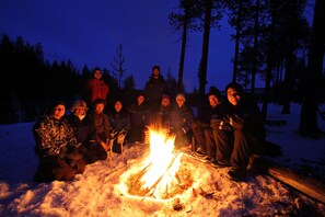 A group of people gathered around a campfire in a snowy forest at night.